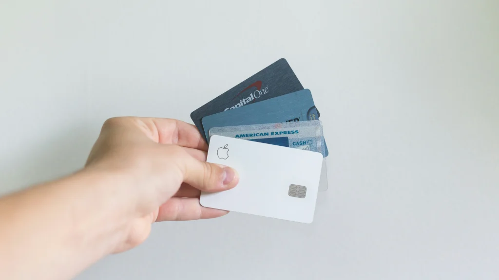 Hand holding multiple credit cards, including Apple, Capital One, Citi, and American Express cards